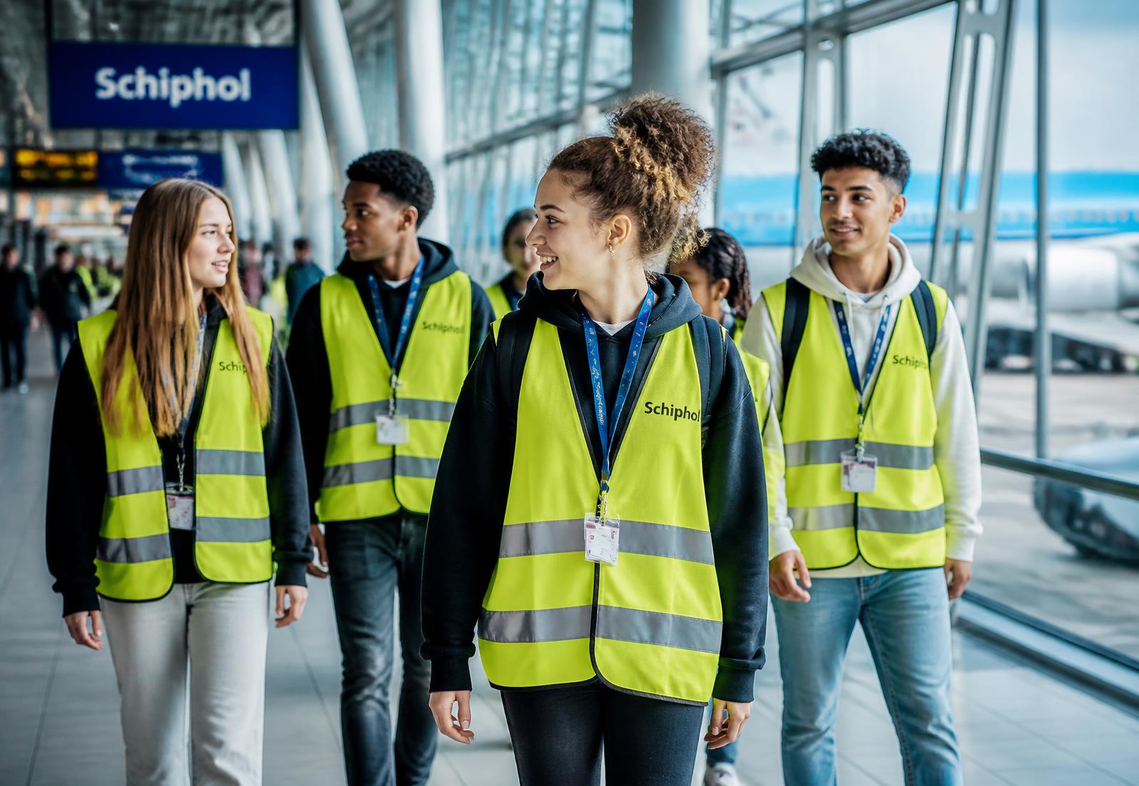 Mladí lidé v reflexních vestách v terminálu letiště Schiphol